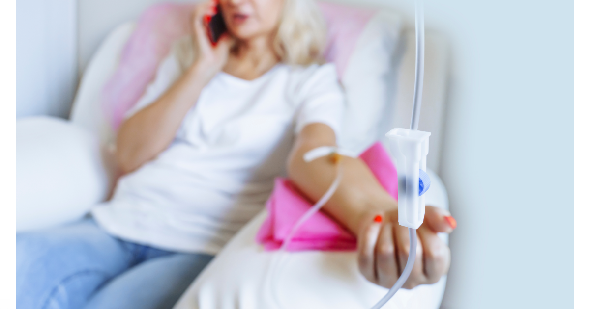 A woman receiving IV therapy while relaxing on a white couch, holding a pink pillow, and talking on the phone. The IV drip and catheter are in focus.