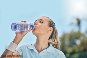 Active woman in a light blue shirt drinking water outdoors under a clear sky, emphasizing hydration and summer wellness.