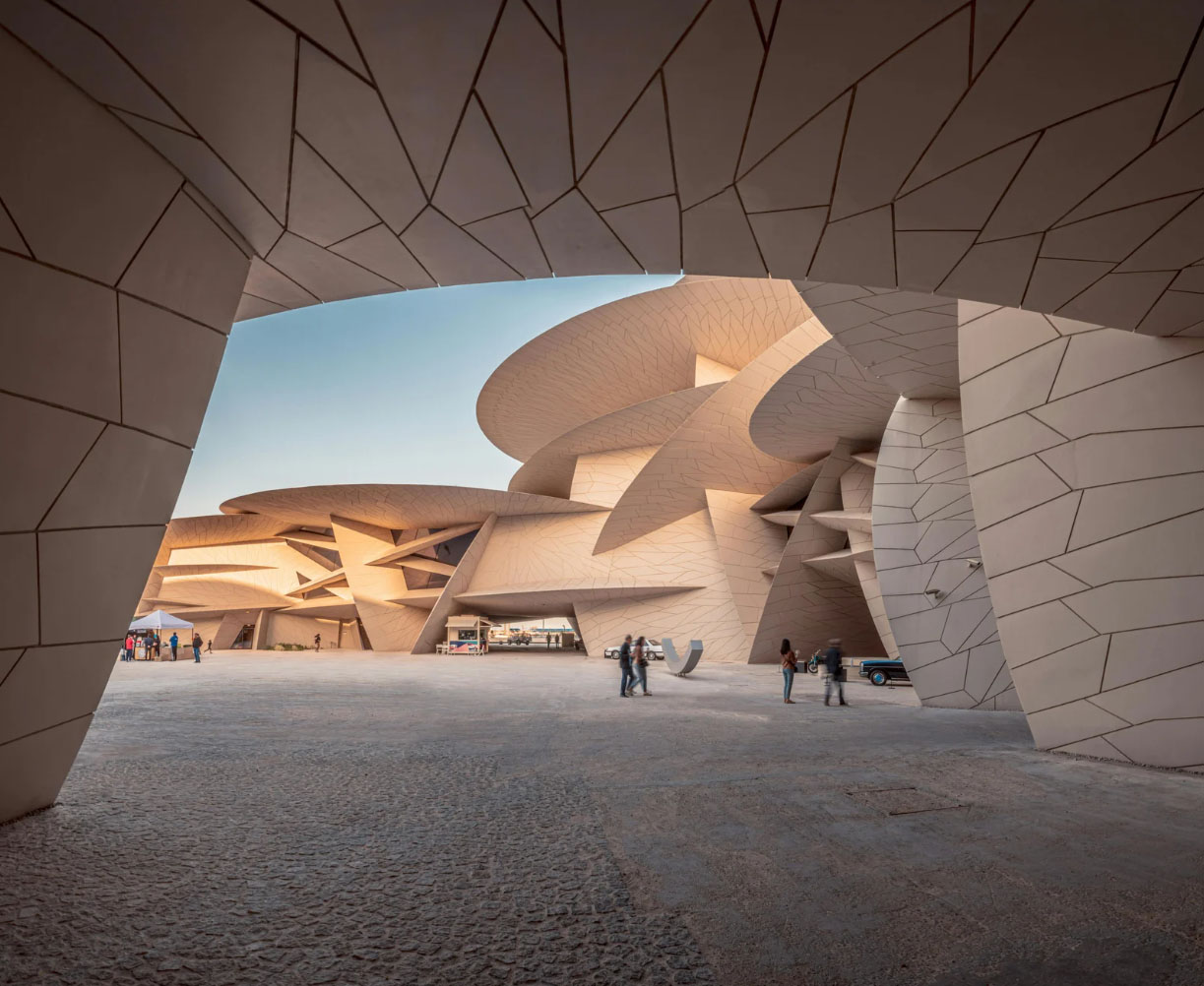 The National Museum of Qatar in Doha, showcasing its striking desert rose-inspired architecture with curved, interlocking disks and a spacious outdoor courtyard with visitors.