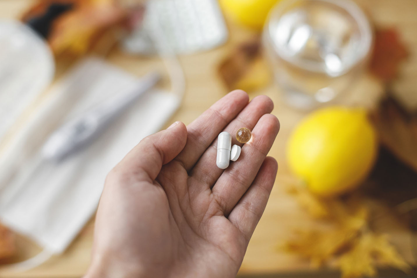 Hand holding Vitamin C and Zinc supplements with lemons, a glass of water, and medical items in the background, symbolizing immune support and wellness.