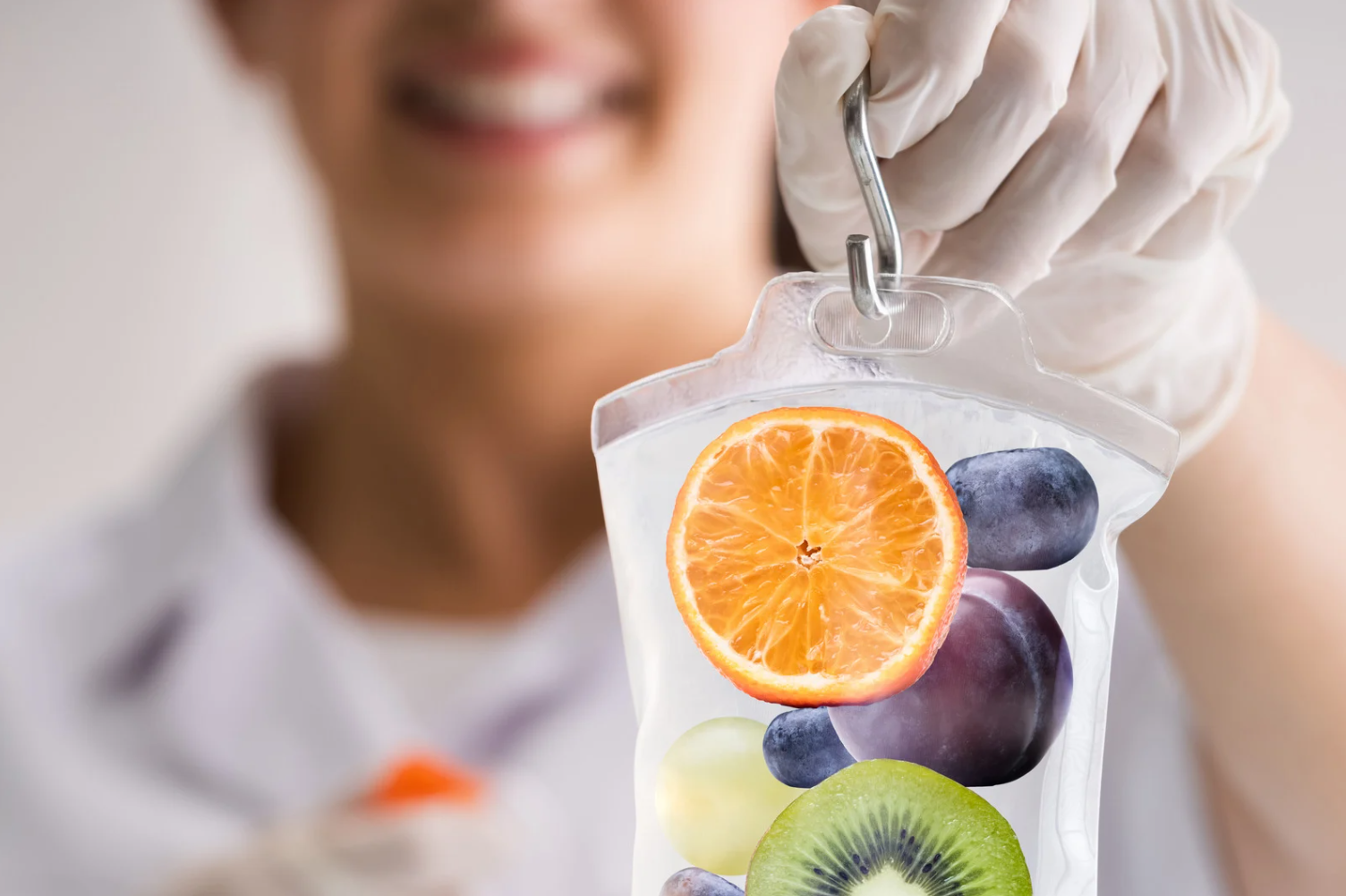 A close-up of a healthcare professional holding an IV bag infused with slices of fruits, including orange, kiwi, and grapes, with a focus on hydration and wellness.