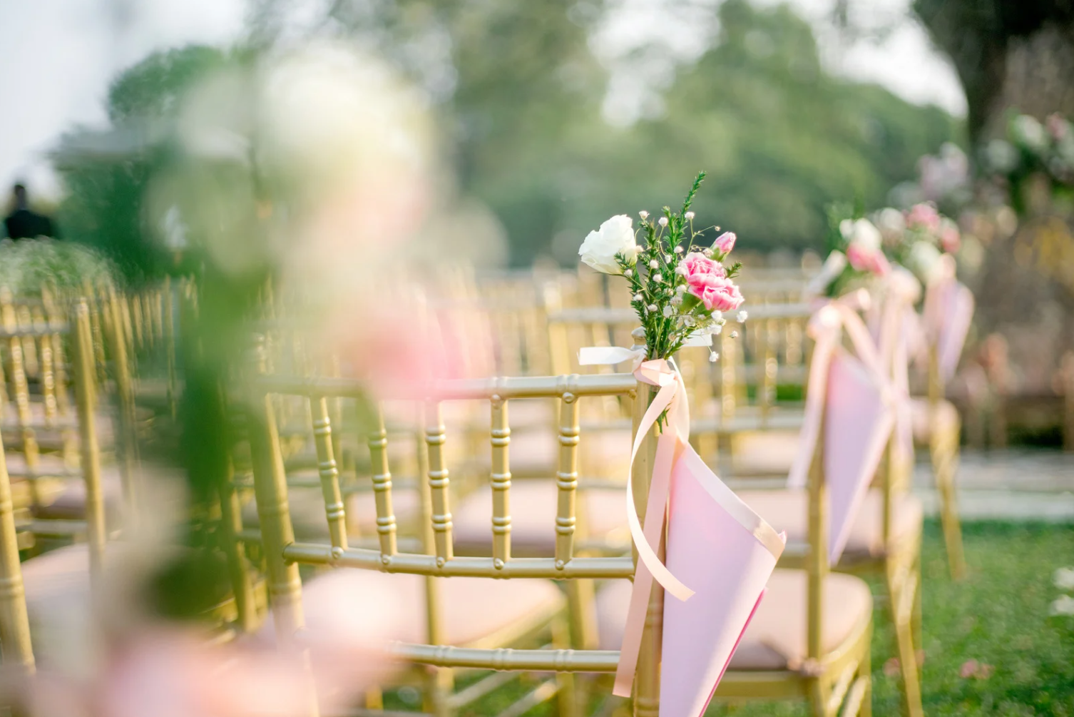 Outdoor wedding ceremony setup with decorated chairs and flowers on ribbons.