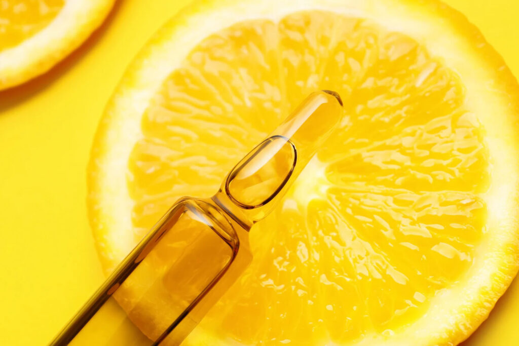 Close-up of a vitamin ampoule placed on top of a fresh orange slice, with a bright yellow background.