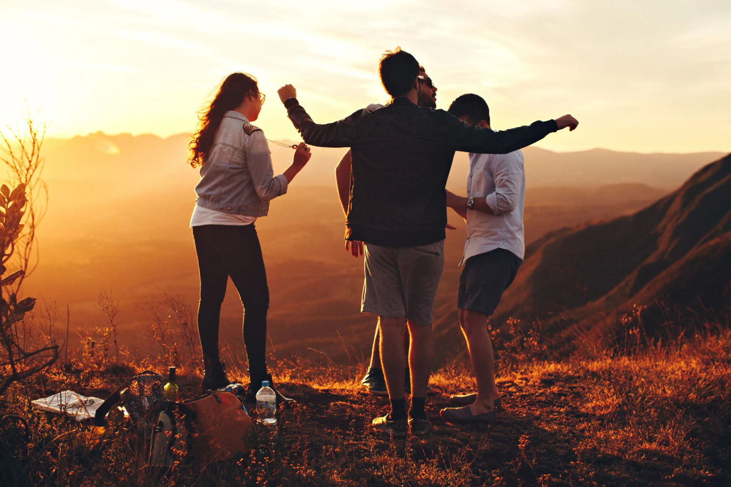 A group of four people dancing together outdoors at sunset, with scenic mountain views in the background.