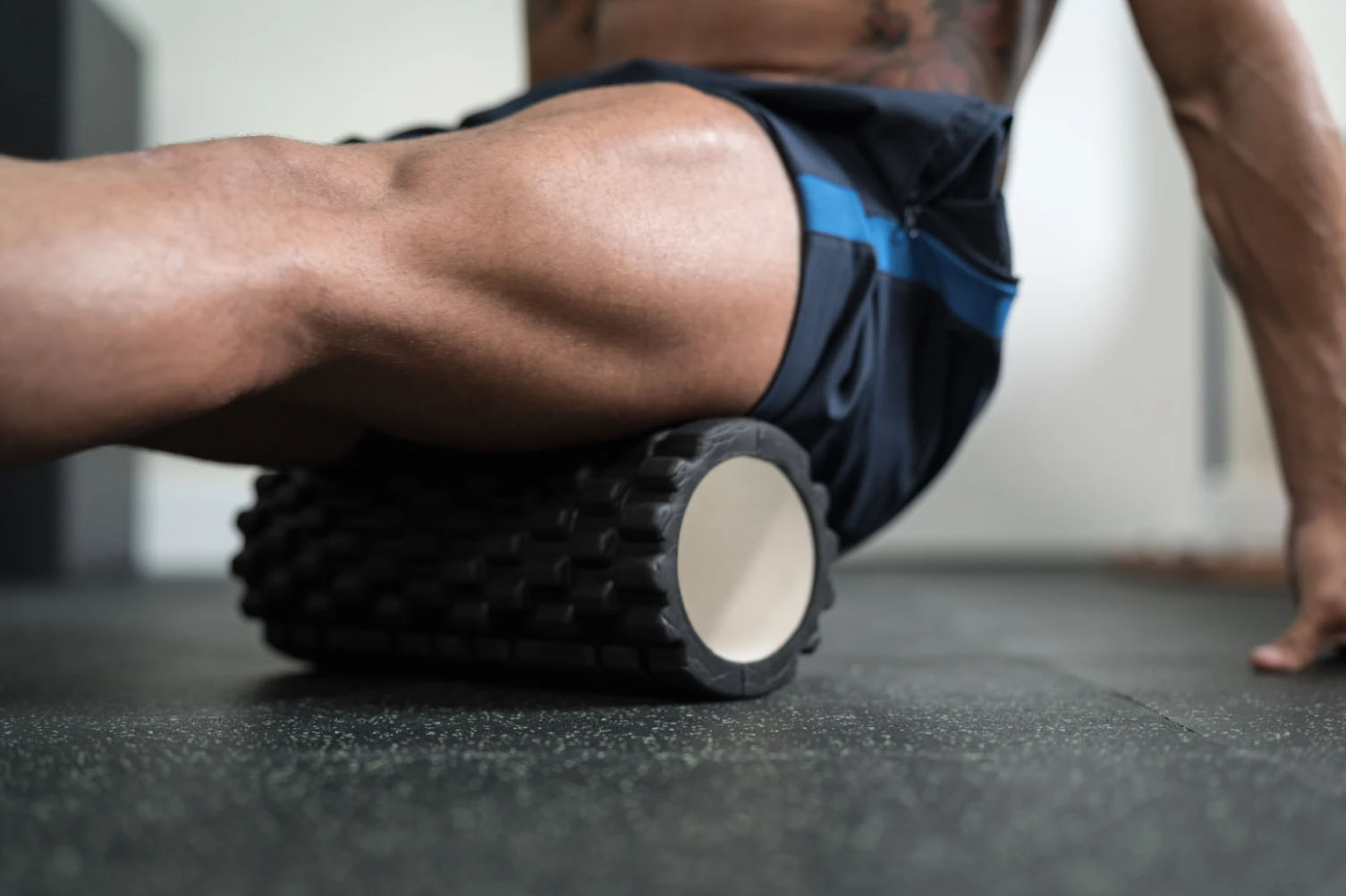A person using a foam roller on their leg while sitting on the floor in a gym or workout space.