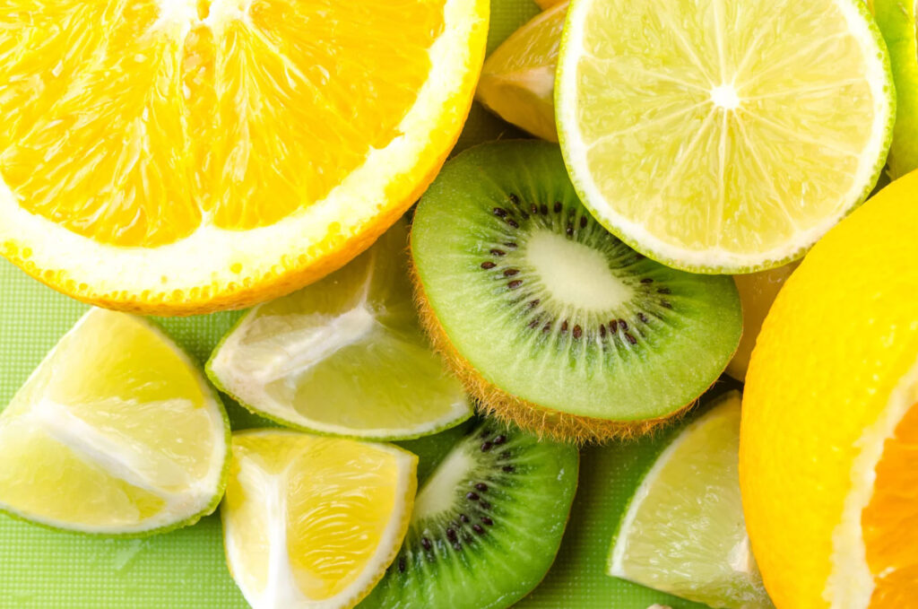 Close-up of sliced fresh fruits including orange, lemon, lime, and kiwi on a green background.
