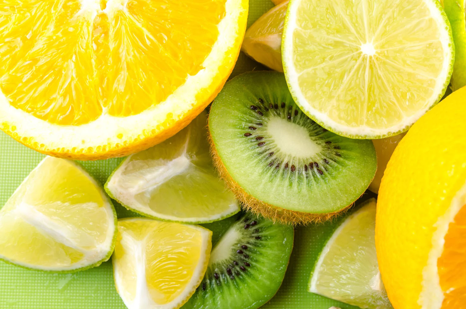 Close-up of sliced fresh fruits including orange, lemon, lime, and kiwi on a green background.