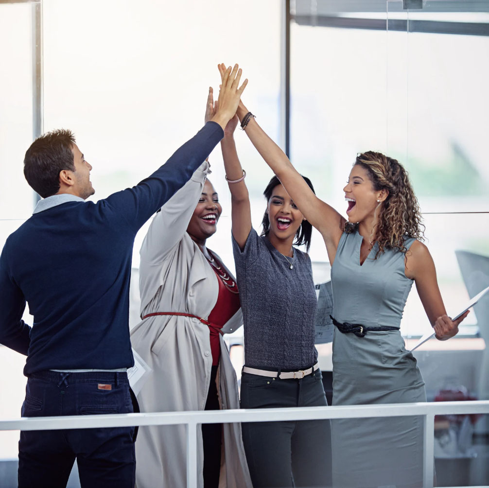 Four diverse colleagues celebrating with high-fives in an office setting, expressing joy and teamwork.
