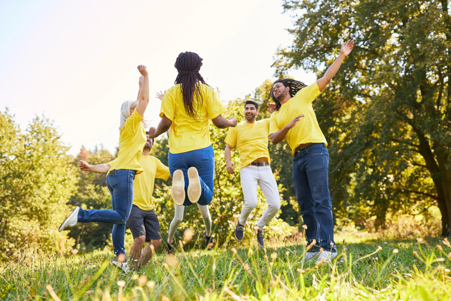 Group of coworkers in yellow shirts jumping and celebrating together outdoors during a team-building event.
