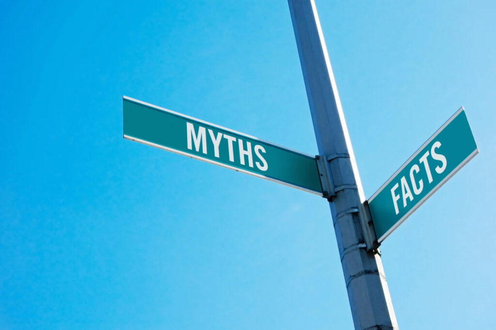 A street signpost pointing in two directions, one labeled "MYTHS" and the other "FACTS," against a bright blue sky background.