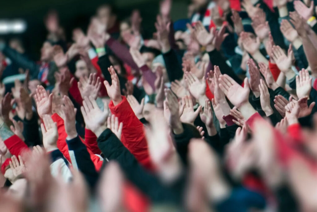 A close-up shot of a crowd at a sporting event, with fans raising their hands in celebration, creating a sense of excitement and unity in the stadium.