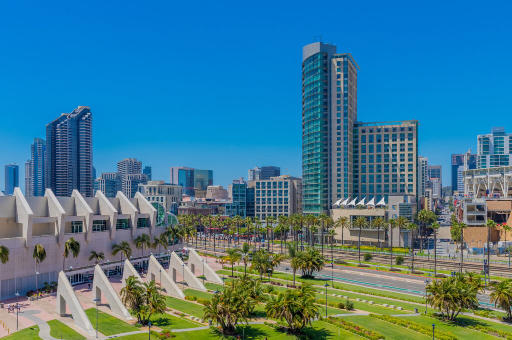 A vibrant view of downtown San Diego, showcasing modern skyscrapers and the San Diego Convention Center with palm trees lining the streets under a clear blue sky.