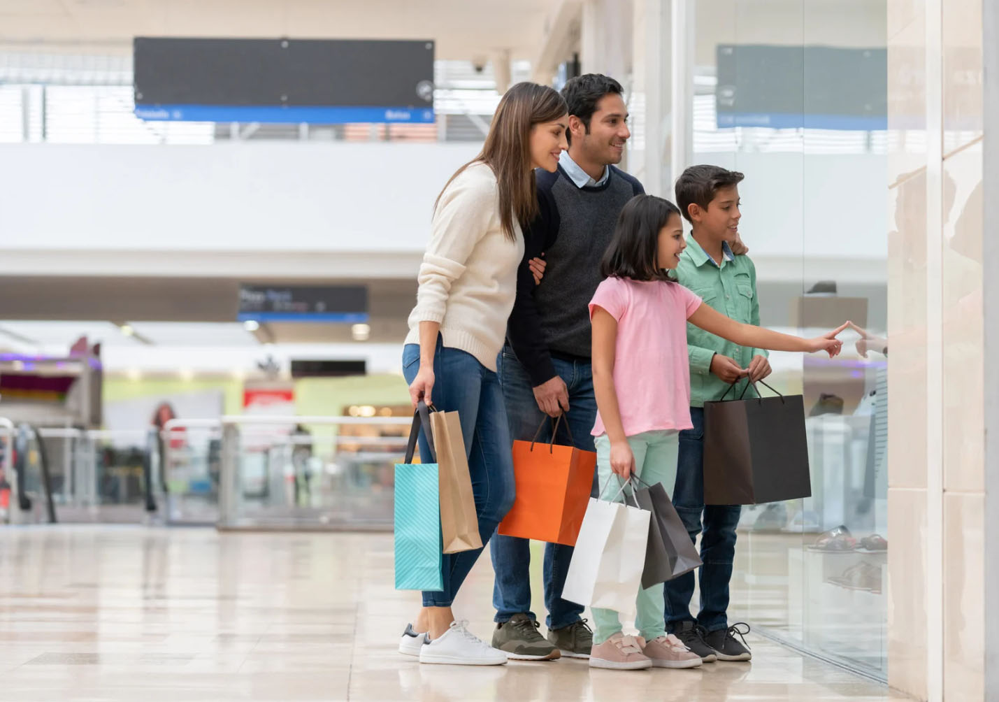 A family of four enjoys shopping together at a mall, holding shopping bags while admiring a store display, capturing a moment of fun and bonding.